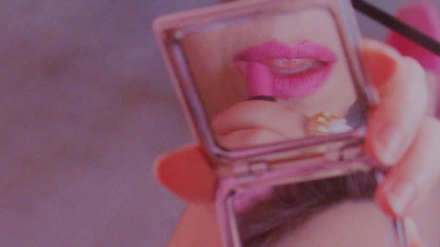 Woman looking at a compact while applying pink lipstick