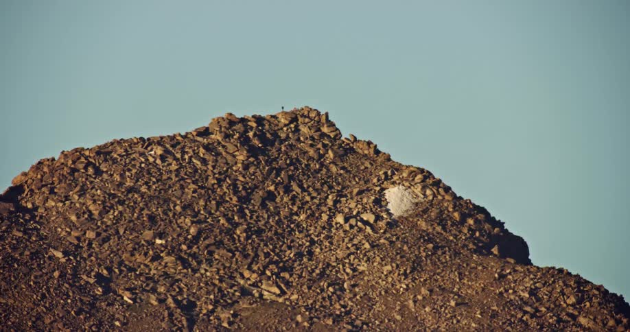 The peak and rocky slopes of a barren mountain under a blue sky