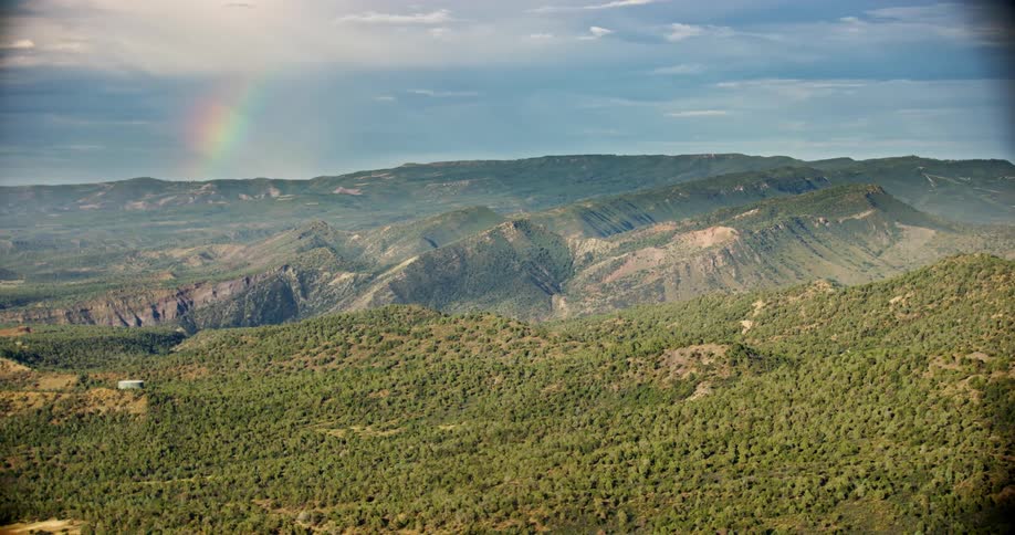 Aerial view of greenish hills and mountains with vegetation and the rainbow in the background on the horizon
