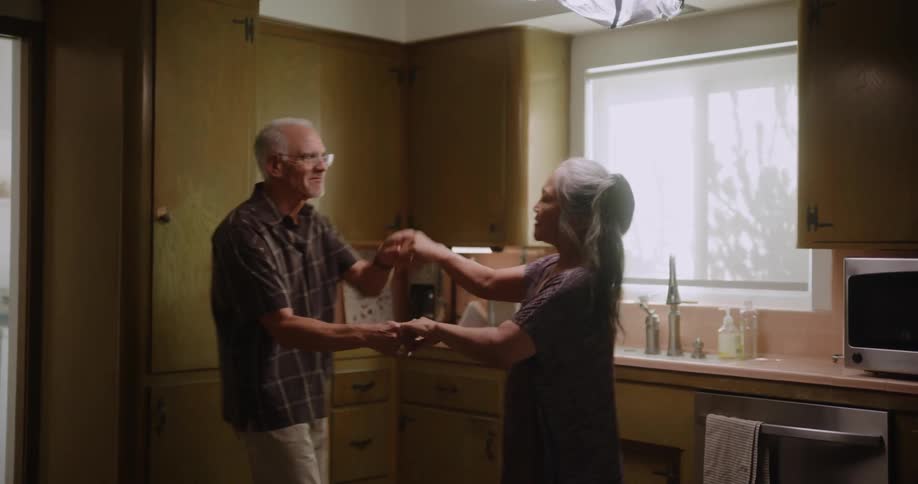 An elderly couple dances in a kitchen