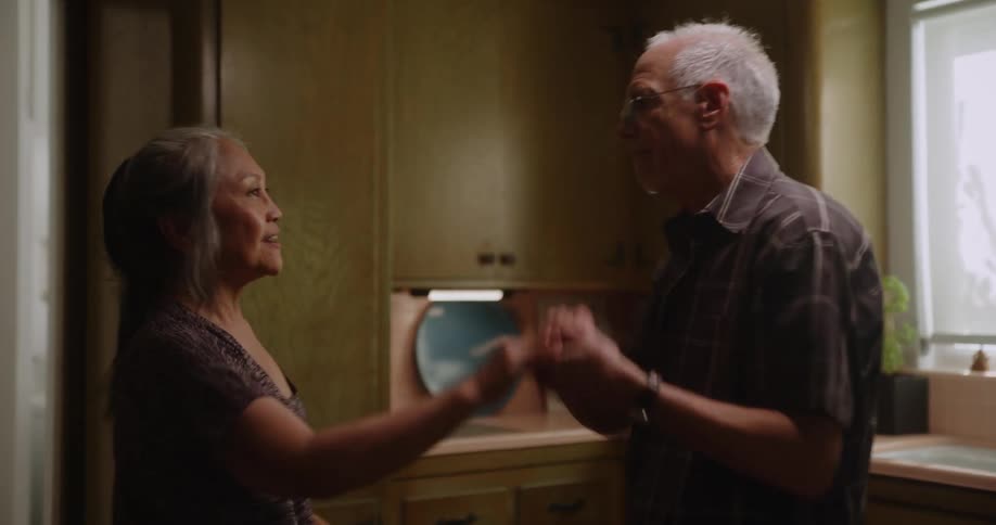 Elderly wife and husband dancing together in their kitchen