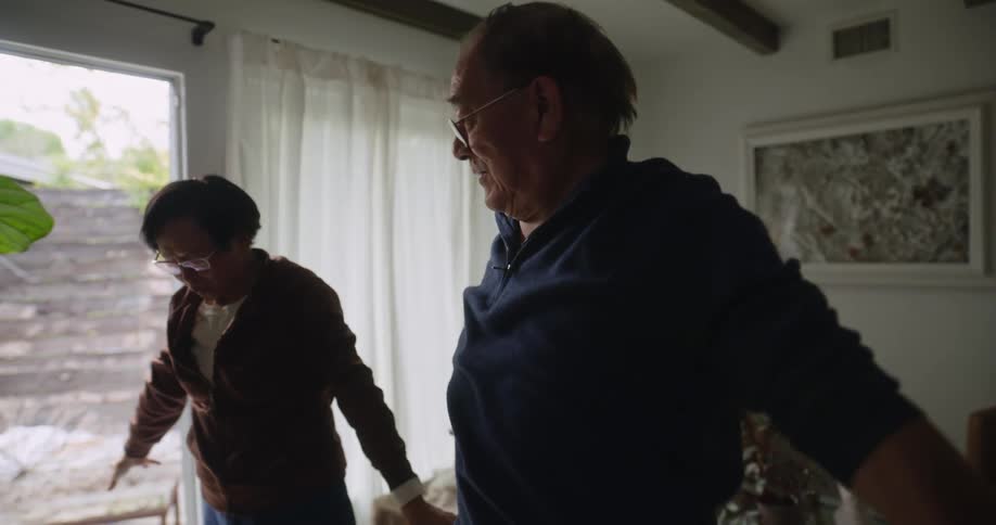 Elderly couple smiles while exercising together in living room