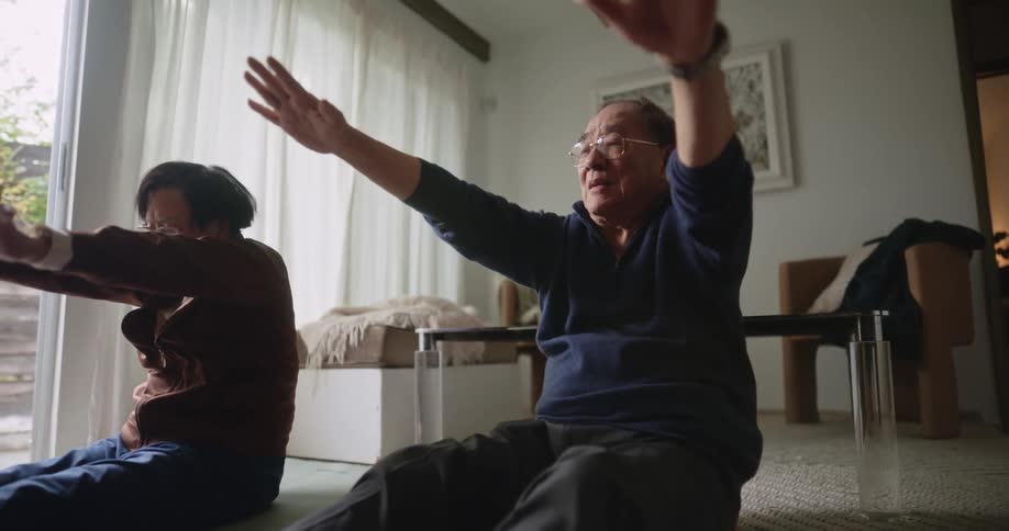 Elderly asian couple stretching on the floor in thier living room
