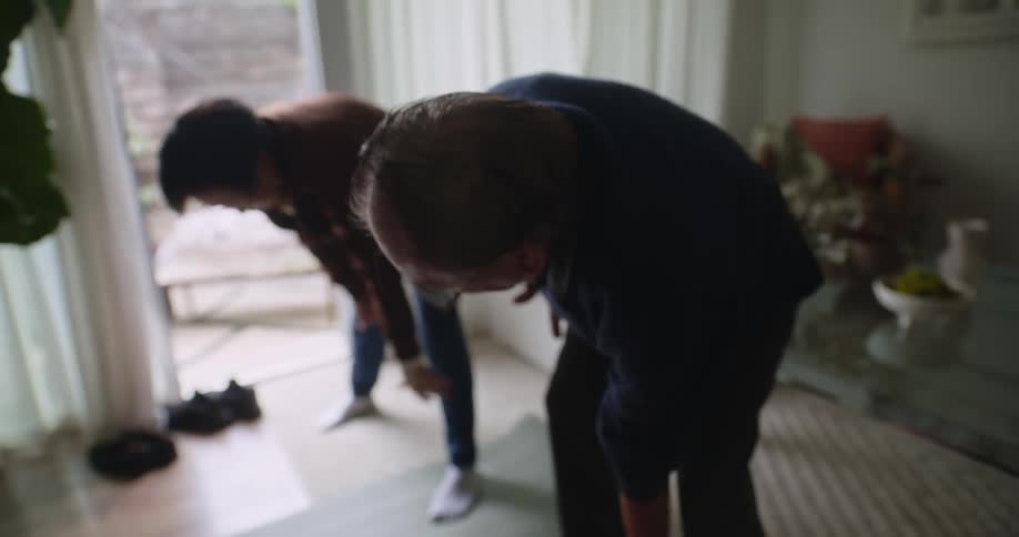Elderly couple in their living room stretching their bodies while the man imitates the tai chi movements that his wife does