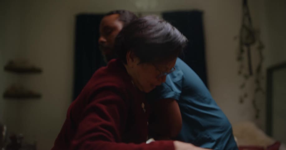A healthcare worker helps an old woman out of a chair