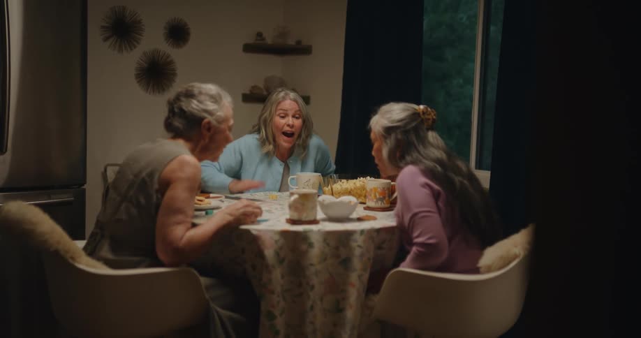 Three happy older women sitting at a round table playing dice