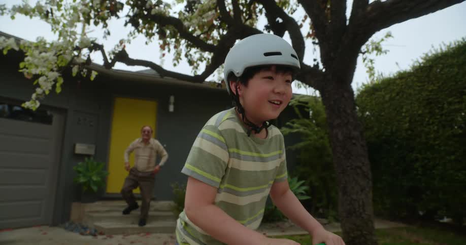 Young boy riding a scooter as his grandfather watches from the steps