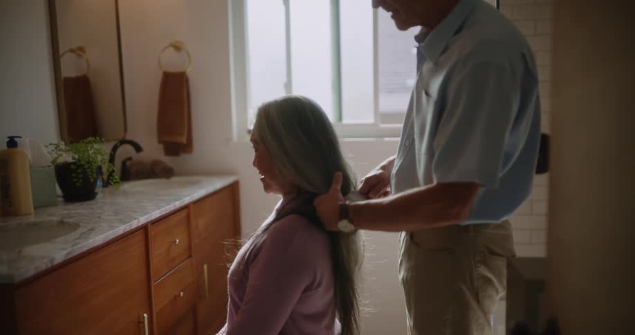 Elderly husband lovingly brushing his wifes long hair in the bathroom