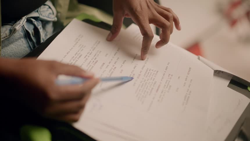 Closeup of a womans hands with a pen reading a script on a paper