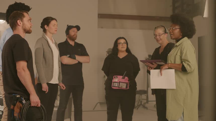 Group of people including men and women cameramen and screenwriters talking to each other inside a studio