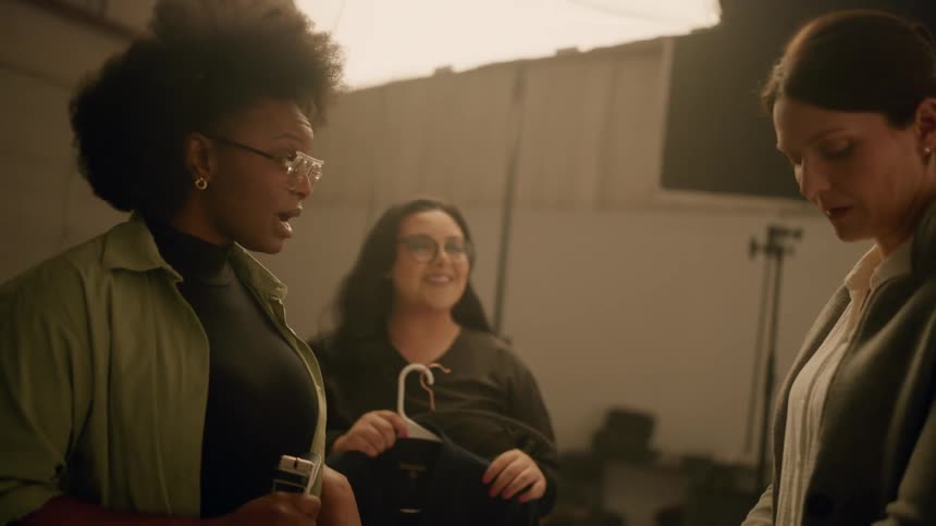 Women inside a studio talking and holding clothes to a model