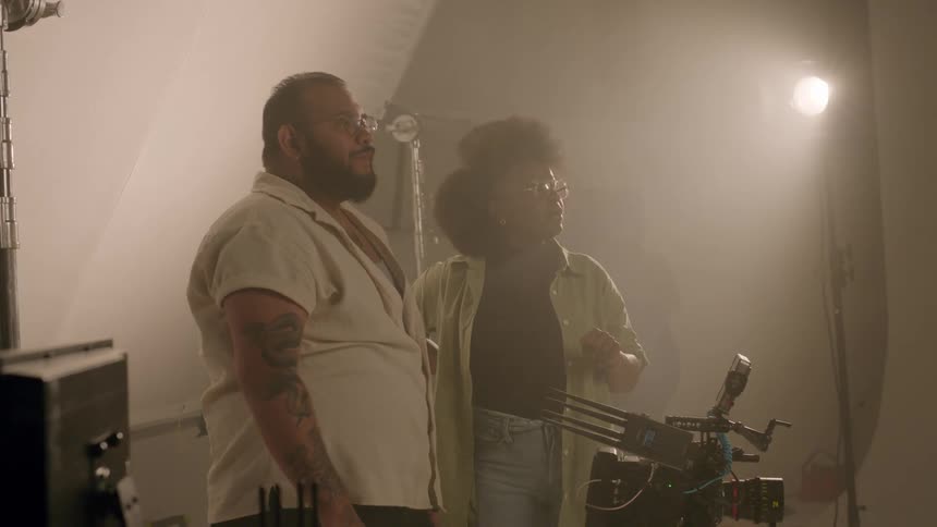 A man in a hazy studio points and asks questions while a woman answers and gives him direction