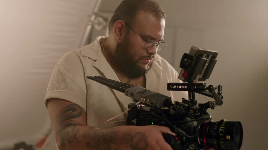 Male photographer adjusts camera lens and looks at display while standing in studio