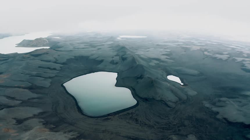 Craters covered by crystal clear water amidst black hills and mountains on a cloudy day