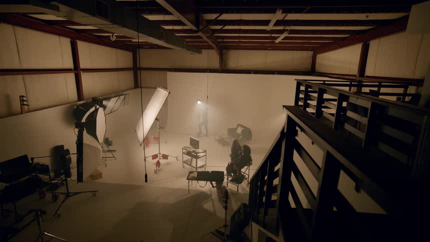 Panorama of an indoor studio with warm light and one woman applying makeup to another