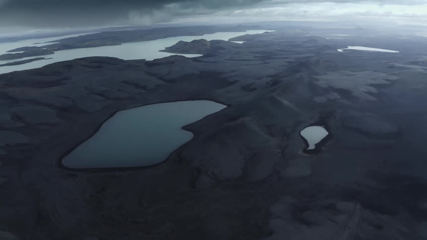 Aerial landscape of mountains with black soils with water basins and ocean around on a sky day with black clouds