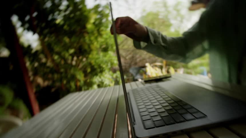 Womans hand opening a laptop on a table on the porch at home