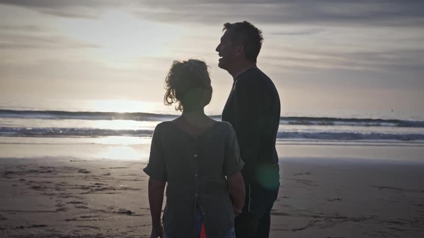 A couple stand on the beach looking at the sunset
