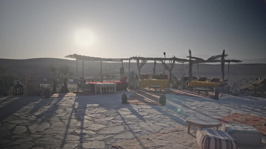 Armchairs and tables in the desert with the sun on the horizon