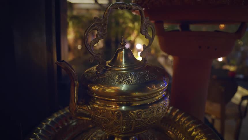 A brass teapot with a floral design sits on a metal tray