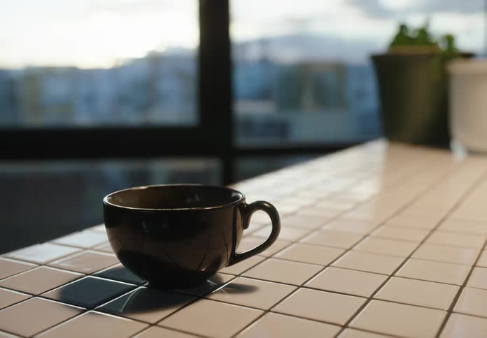A black ceramic coffee cup sits on a white tiled countertop