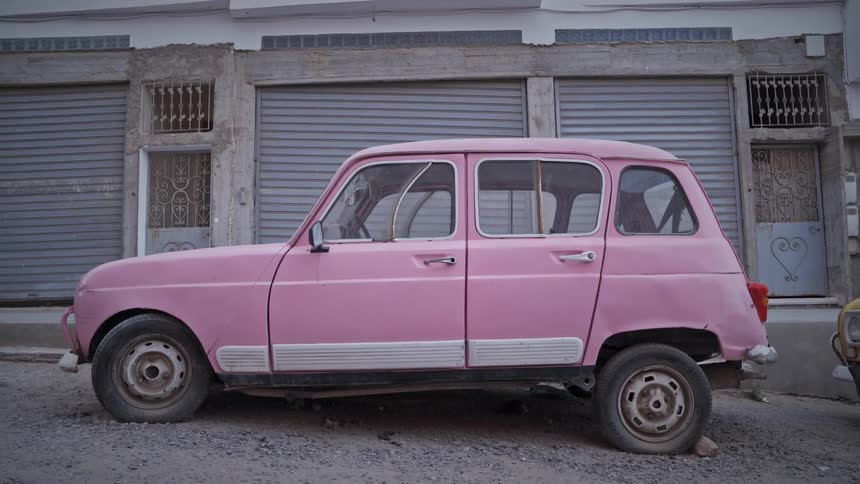 A pink car is parked by a building during the day time