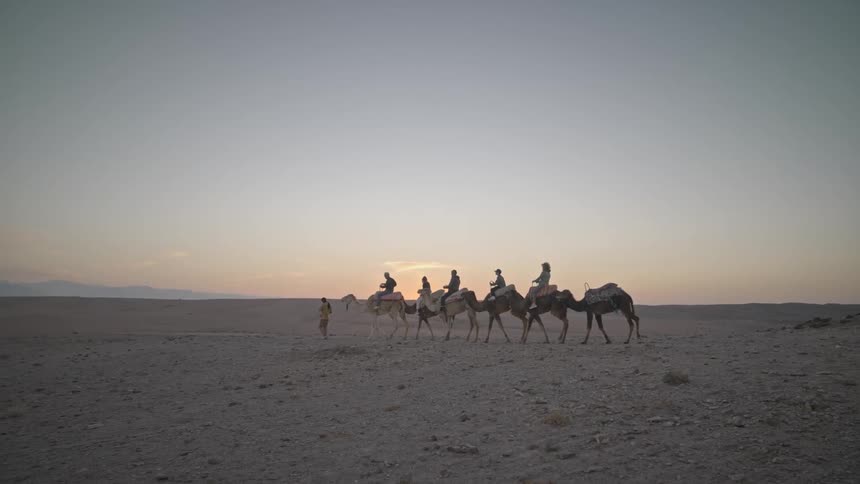 A group of people are riding camels along a dirt path in a vast desert