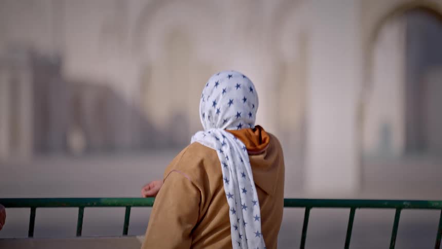 Back view of a woman leaning on a handrail wearing a hijab