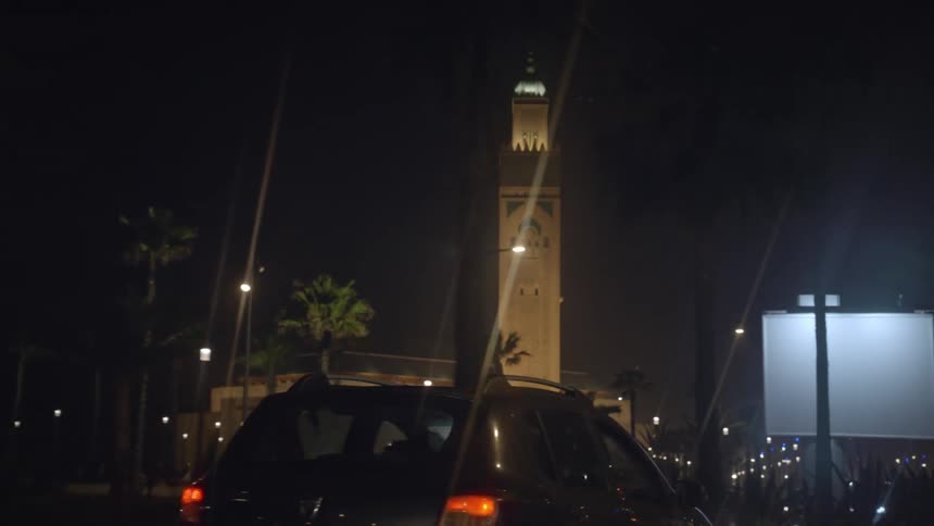 Exterior of a street at night with a view of a huge tower of a majestic mosque