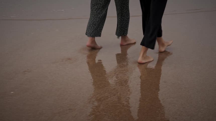 Two people are walking barefoot together on the beach