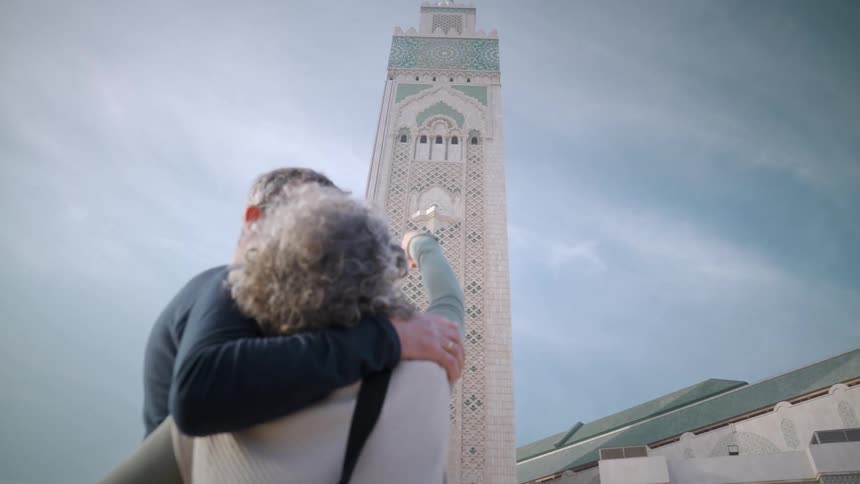 An elderly couple in front of a mosque they point at the tower talking