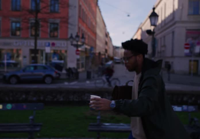 A black man runs down a city sidewalk with a cup and a bag