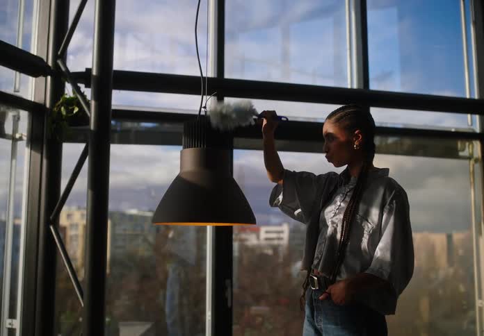 Woman cleaning the chandelier in an office while her colleague calls her and offers her a cappuccino