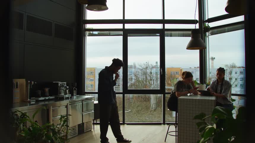 Man in the office cafeteria walking in a circle and next to two women sitting using their cell phone and tablet