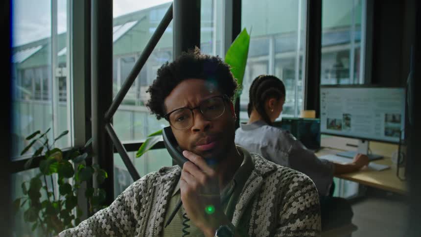 Man talks on the phone while his co worker works on a computer behind him