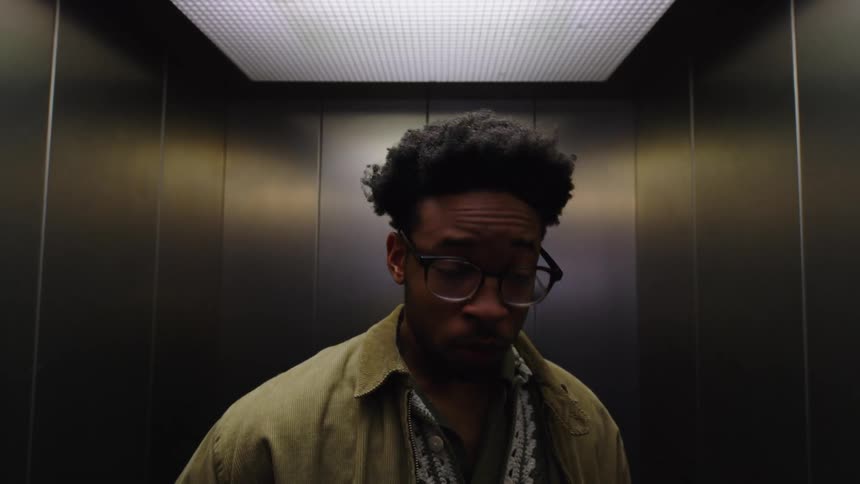 A young man checks his breath on an elevator