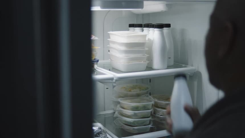 Man opening the refrigerator and taking out a small bottle