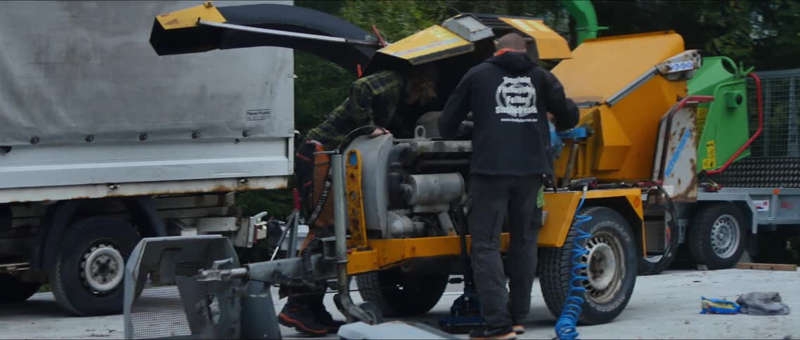 A couple of workers adjusting a yellow woodchipper