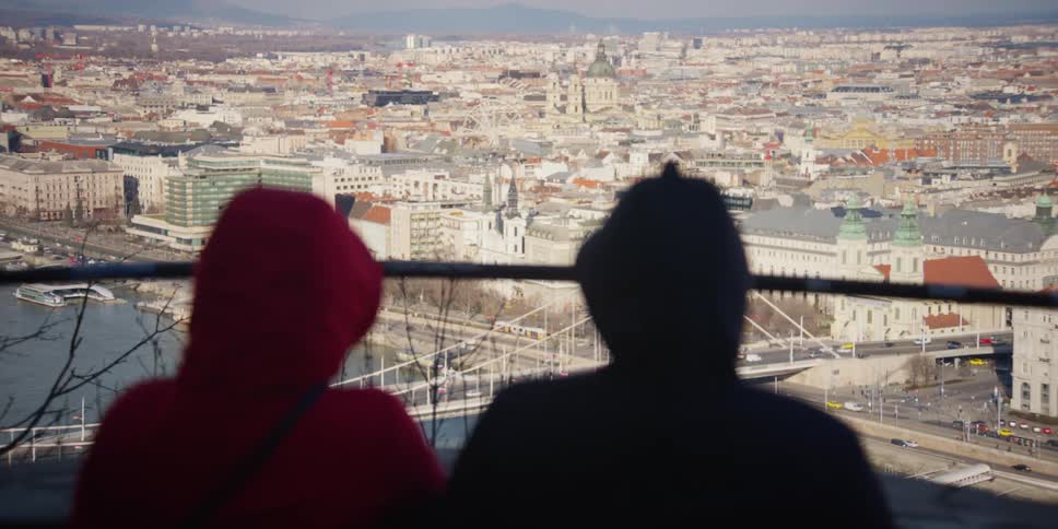 Two people sit near rail overlooking Elizabeth bridge crossing the Danube River on Budapest waterfront