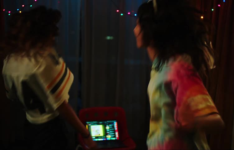 Two teenage girls dancing with hands raised in a dimly lit room with colorful lights