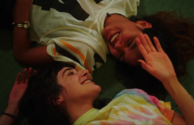 Two young women lying on the carpet looking at each other talking and smiling