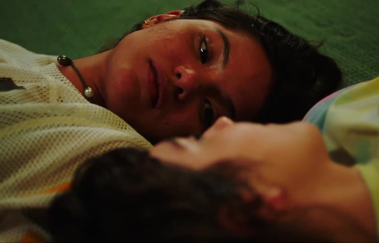 Two young women lying on the floor rug looking at each other romantically and laughing