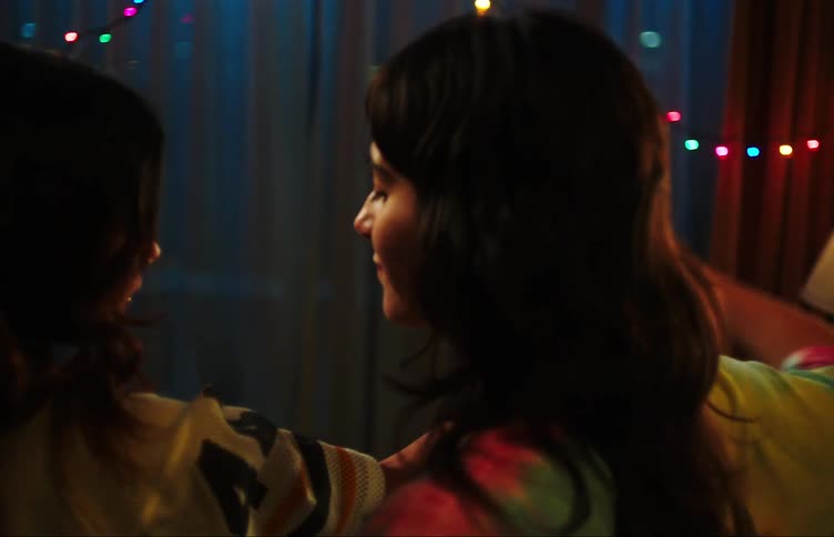 Two teenage girls dancing with hands raised in a dimly lit room with colorful lights