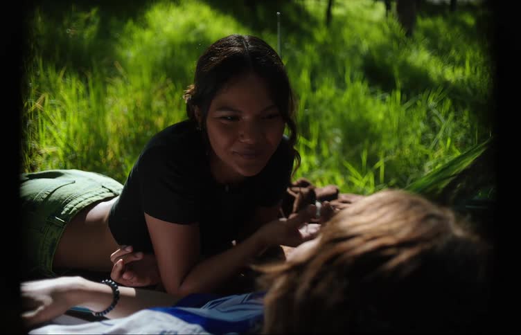 Two female friends hanging out relaxing on the lawn sharing a joint