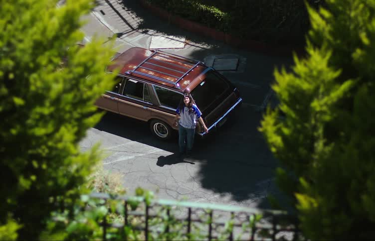 A teenage girl reclined on a car parked on the street waiting for someone