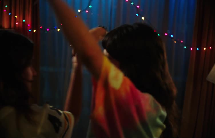 Two teenage girls dancing with hands raised in a dimly lit room with colorful lights