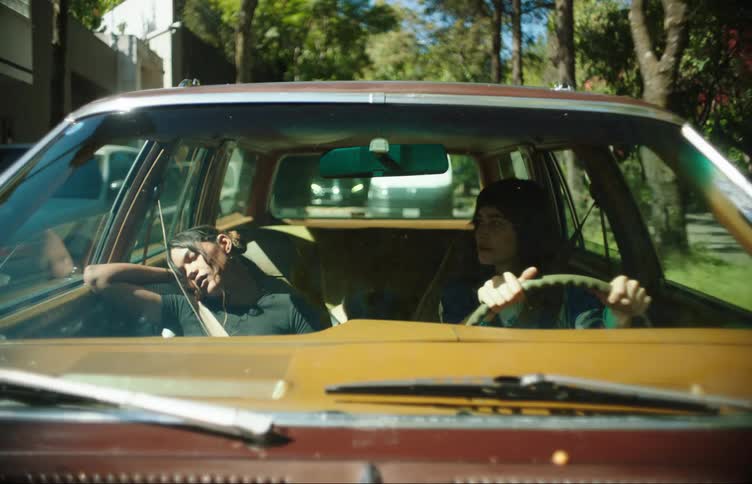Front windshield of a vehicle with a woman driving on an urban road and a young girl sleeping next to her