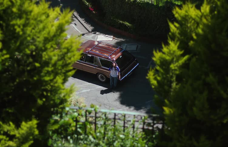 A teenage girl reclined on a car parked on the street waiting for someone