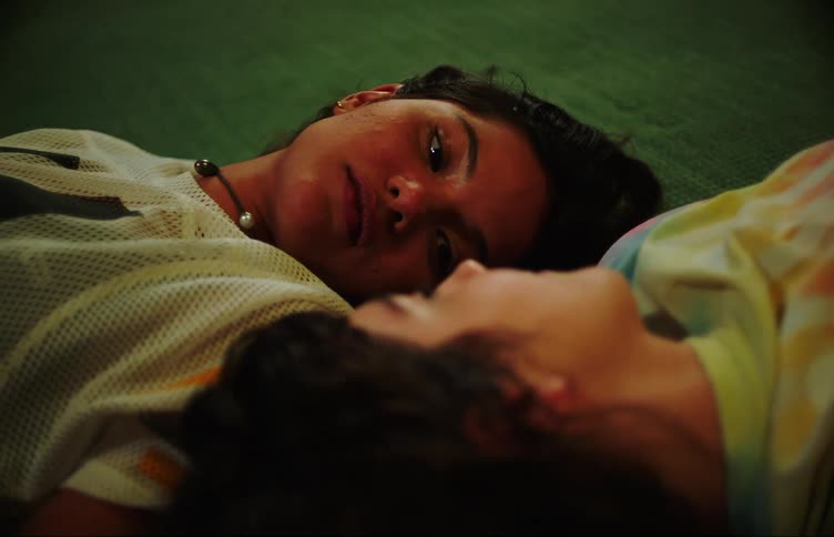 Two young women lying on the floor in opposite directions head to head laughing and smiling at each other