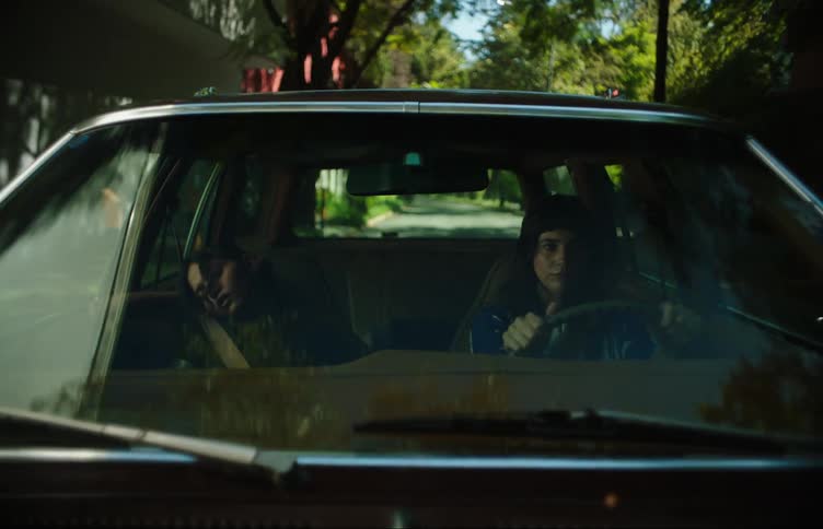 A girl drives a car through the neighborhood while her friend sleeps